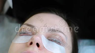美容治疗。 美容师用刷子在卷发器睫毛上涂上一种溶液。 肉毒杆菌和睫毛层压。 闭上眼睛
